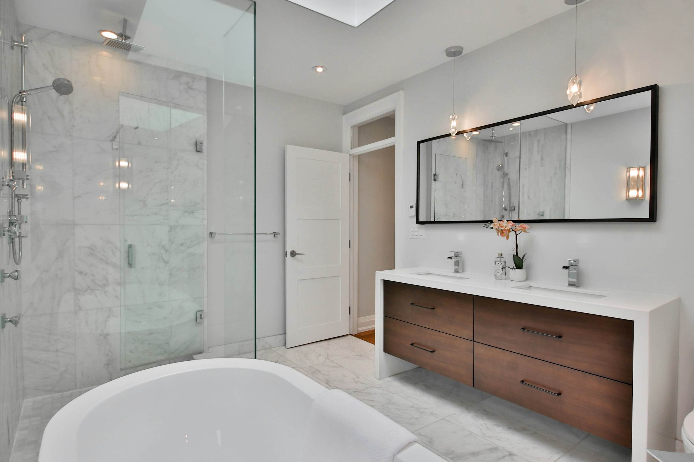 A large freestanding tub beside a walk-in shower with walnut wall panels