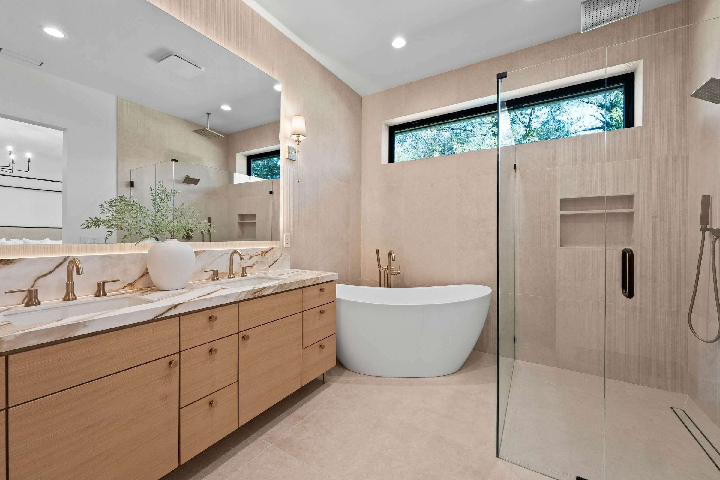 A primary bathroom with a long double vanity, freestanding tub and glass shower