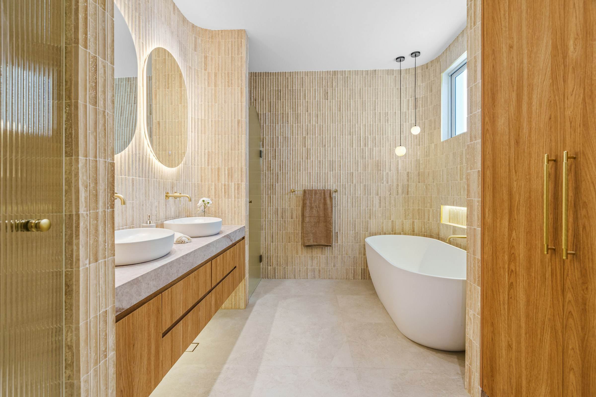 A warm bathroom with oak cabinetry, double basins and a freestanding tub