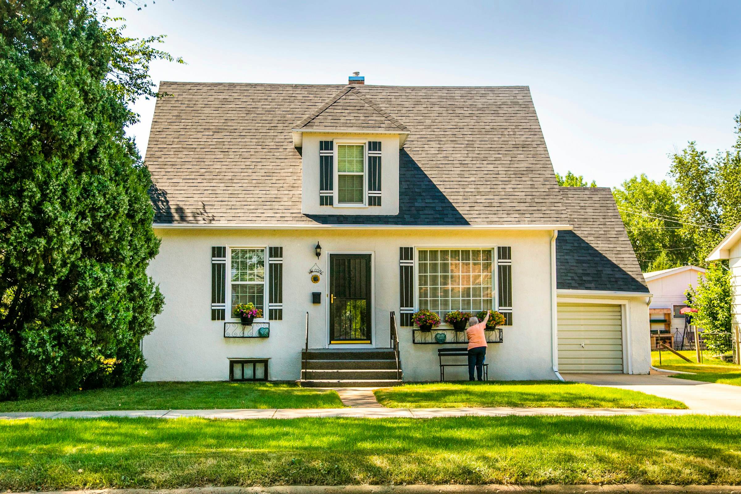 A white Cape Cod style house with a shingle roof and green lawn