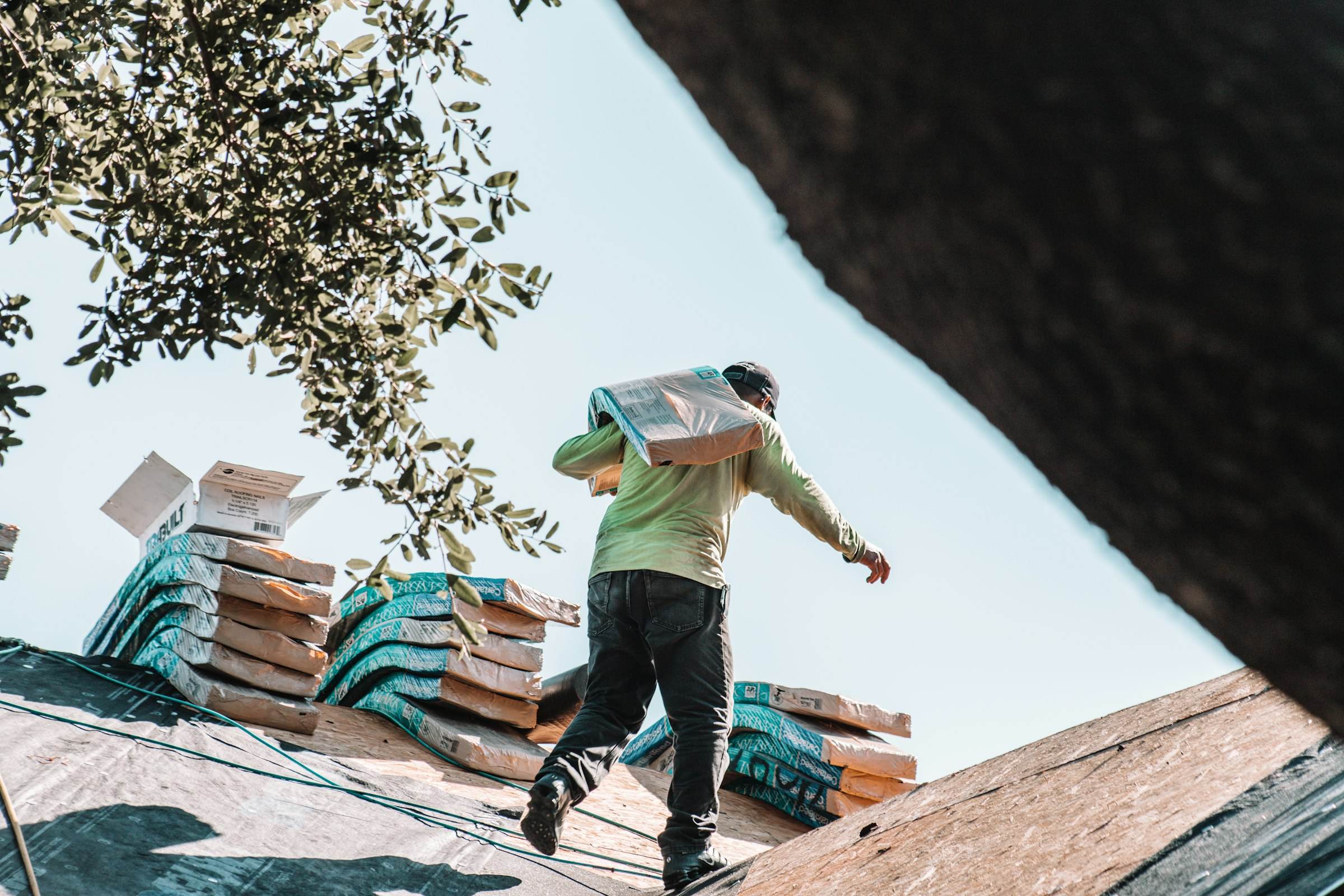 A roofer carrying a bundle of new shingles across a roof deck