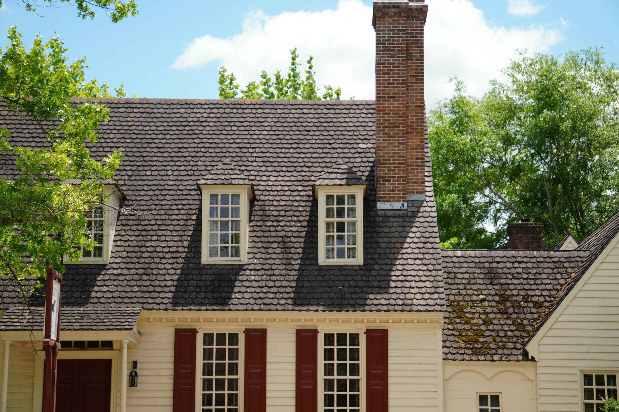 A home with dormers, a brick chimney and a dark shingle roof