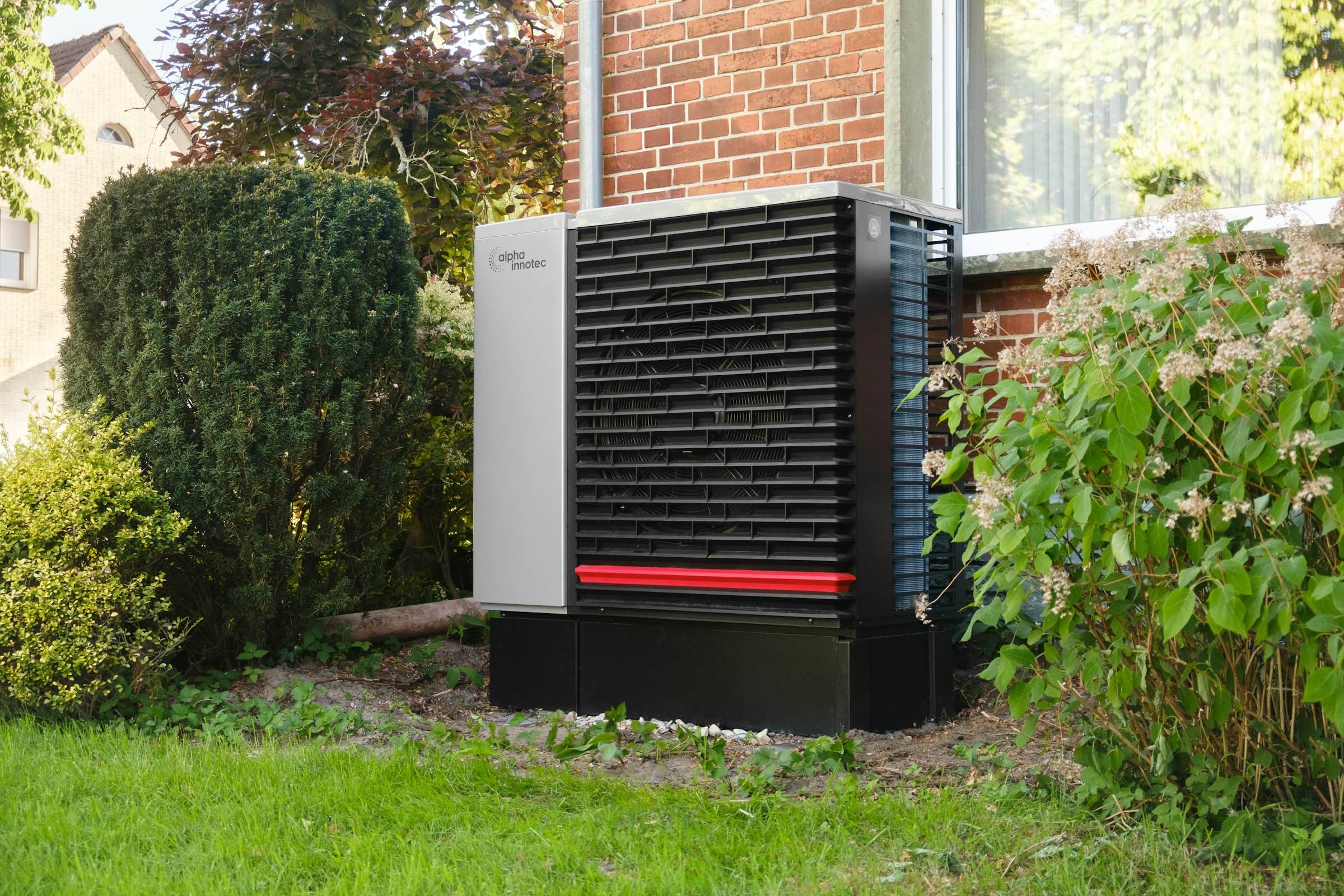 An outdoor heat pump unit beside a brick house and shrubs