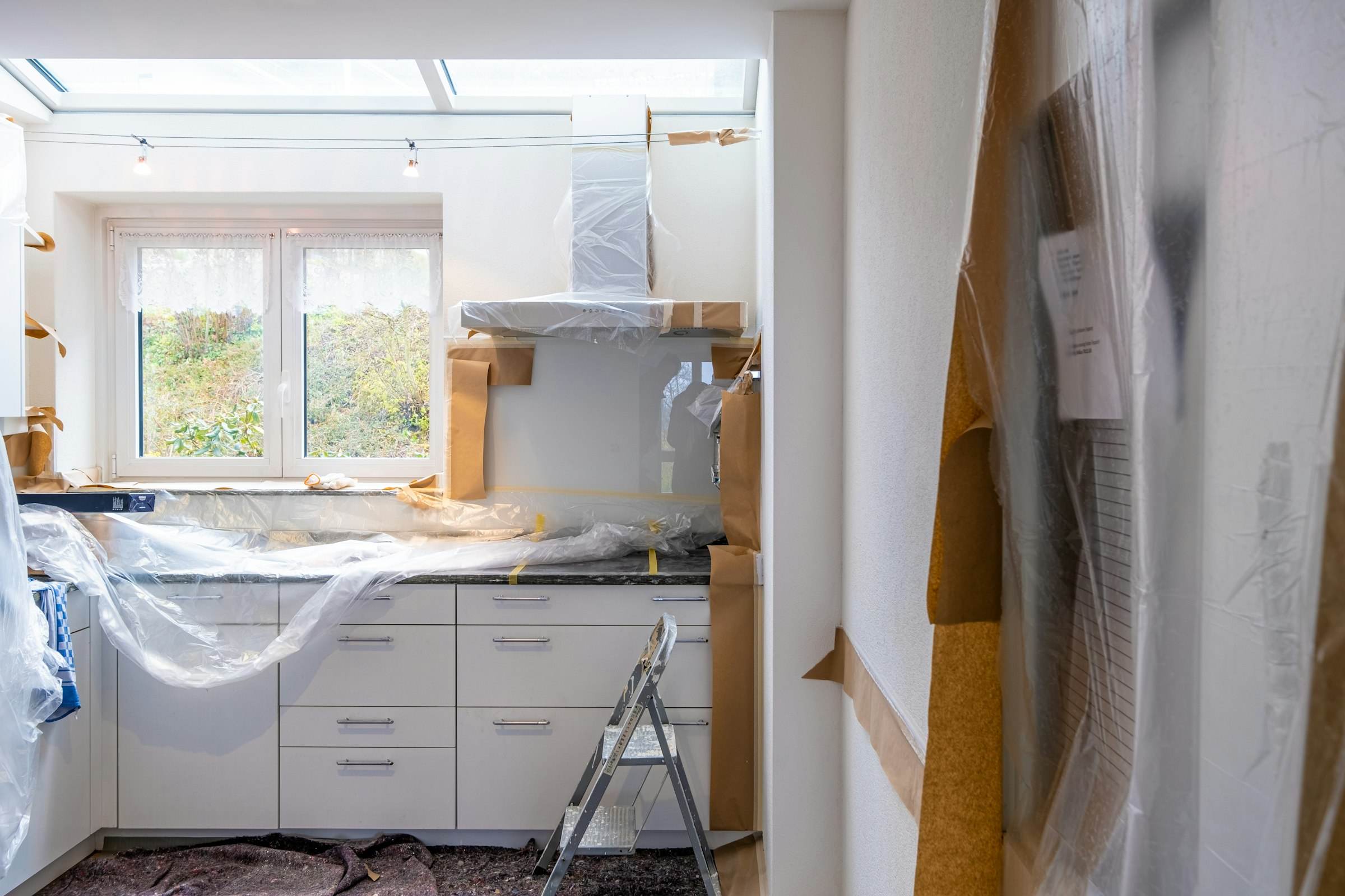 A kitchen mid-renovation, with cabinets wrapped in plastic and floors protected