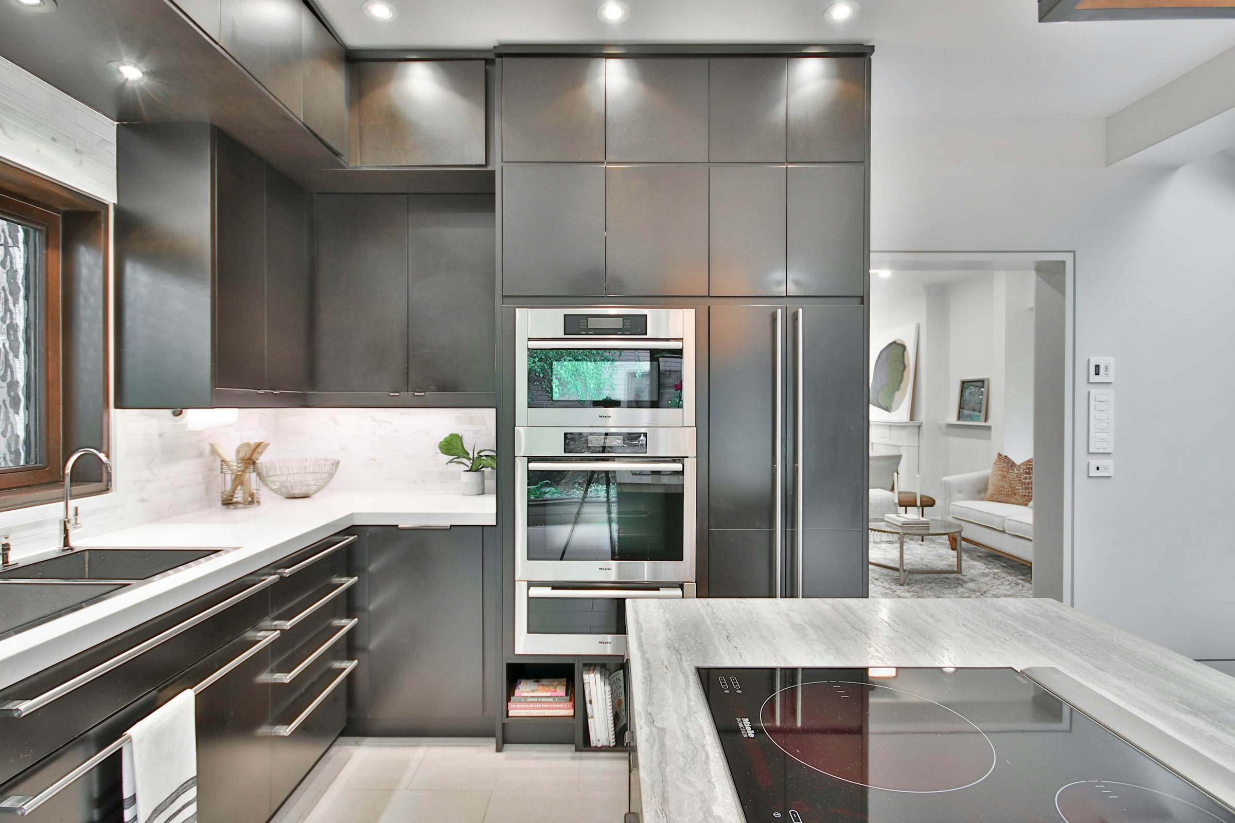A modern kitchen with dark cabinetry, built-in ovens and stone counters