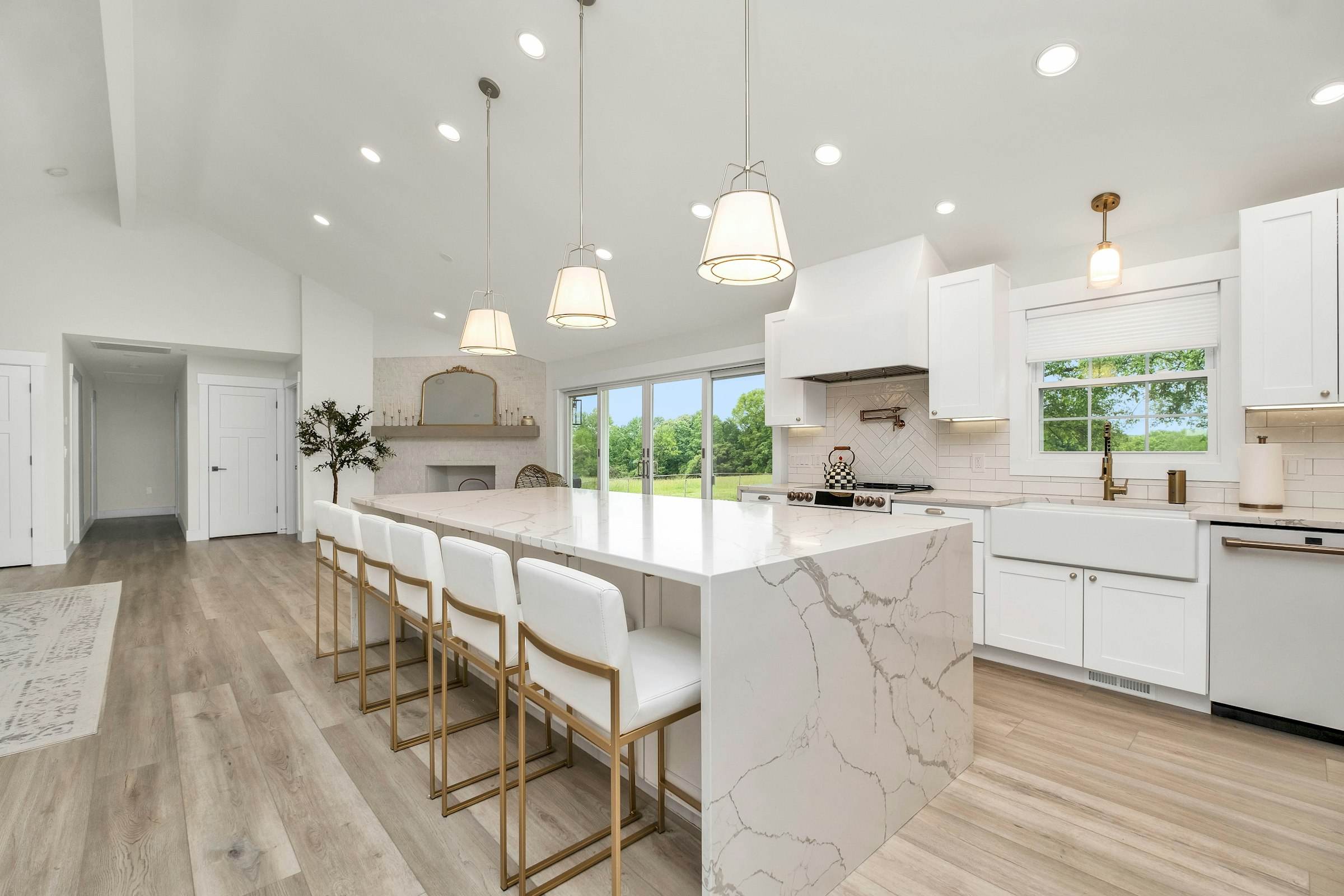 A bright kitchen with a marble waterfall island and brass stools