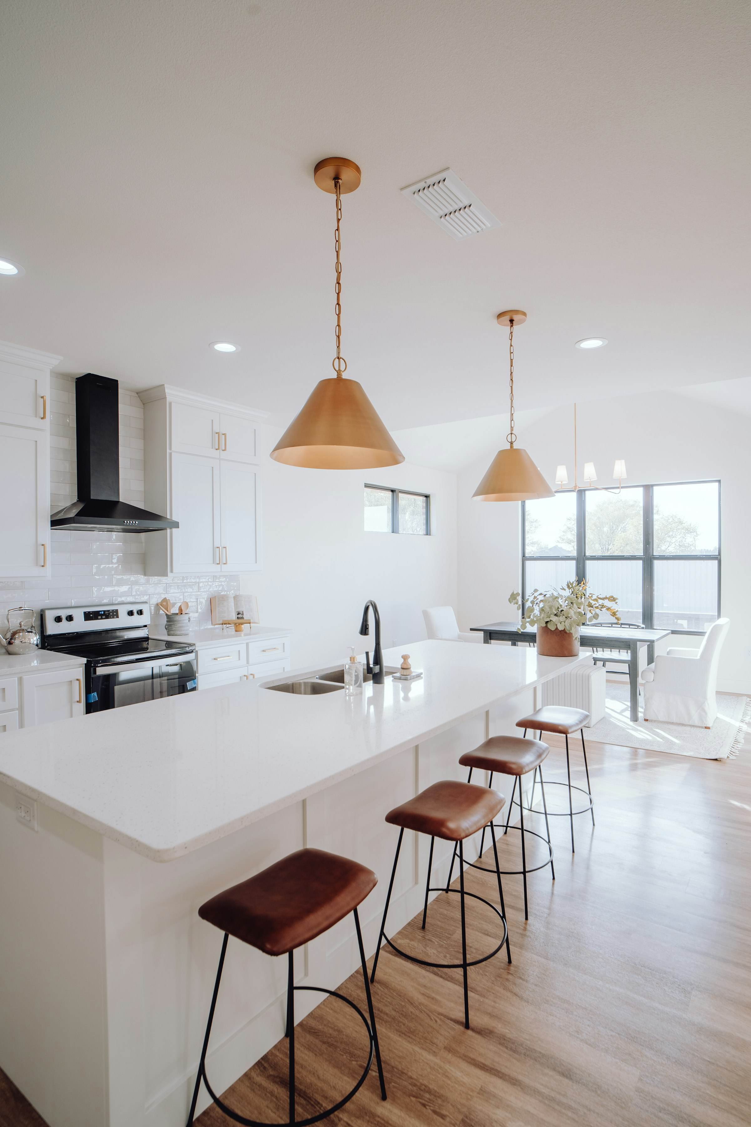 An open kitchen with a long walnut and white island, pendant lights and garden views