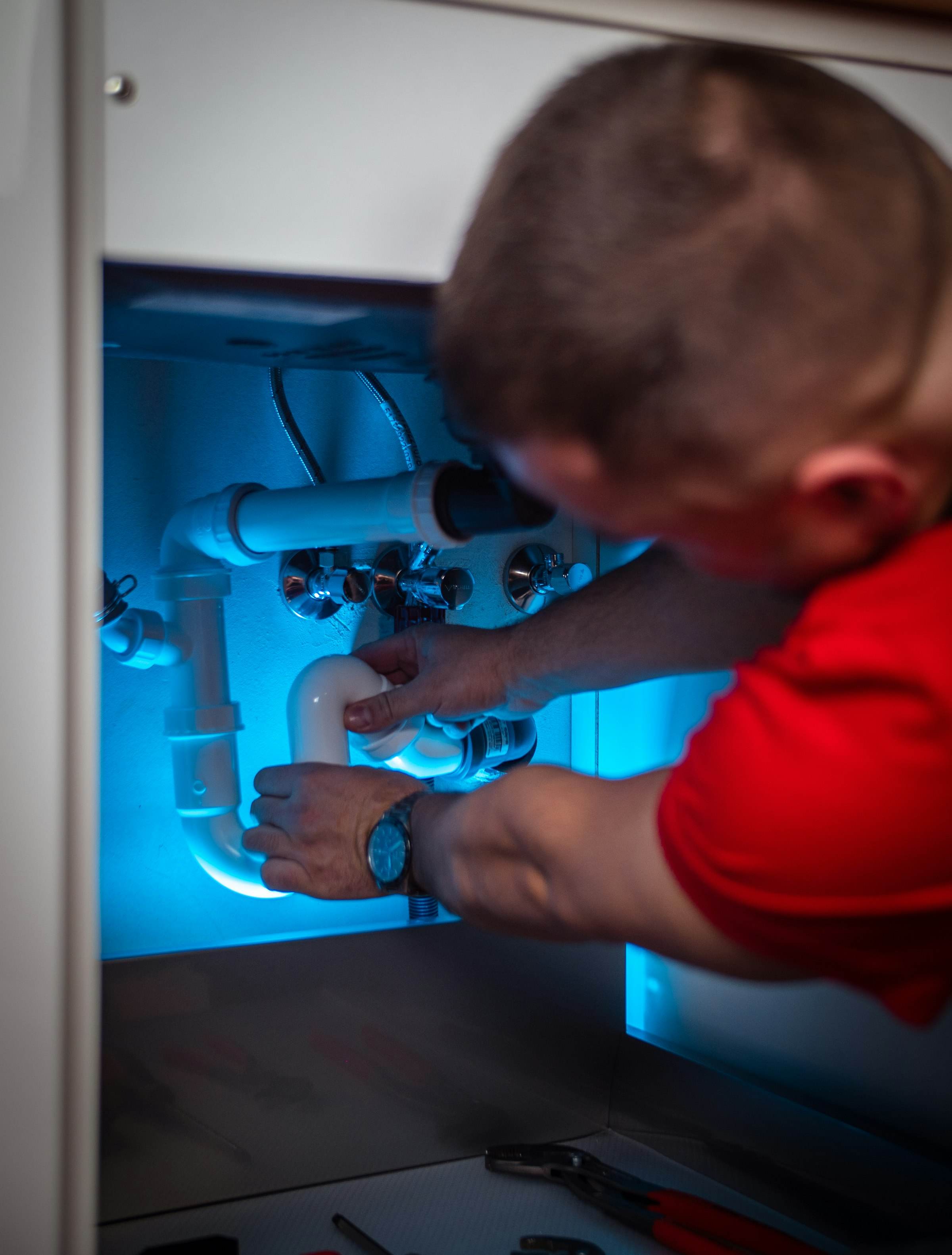A plumber tightening fittings under a bathroom basin