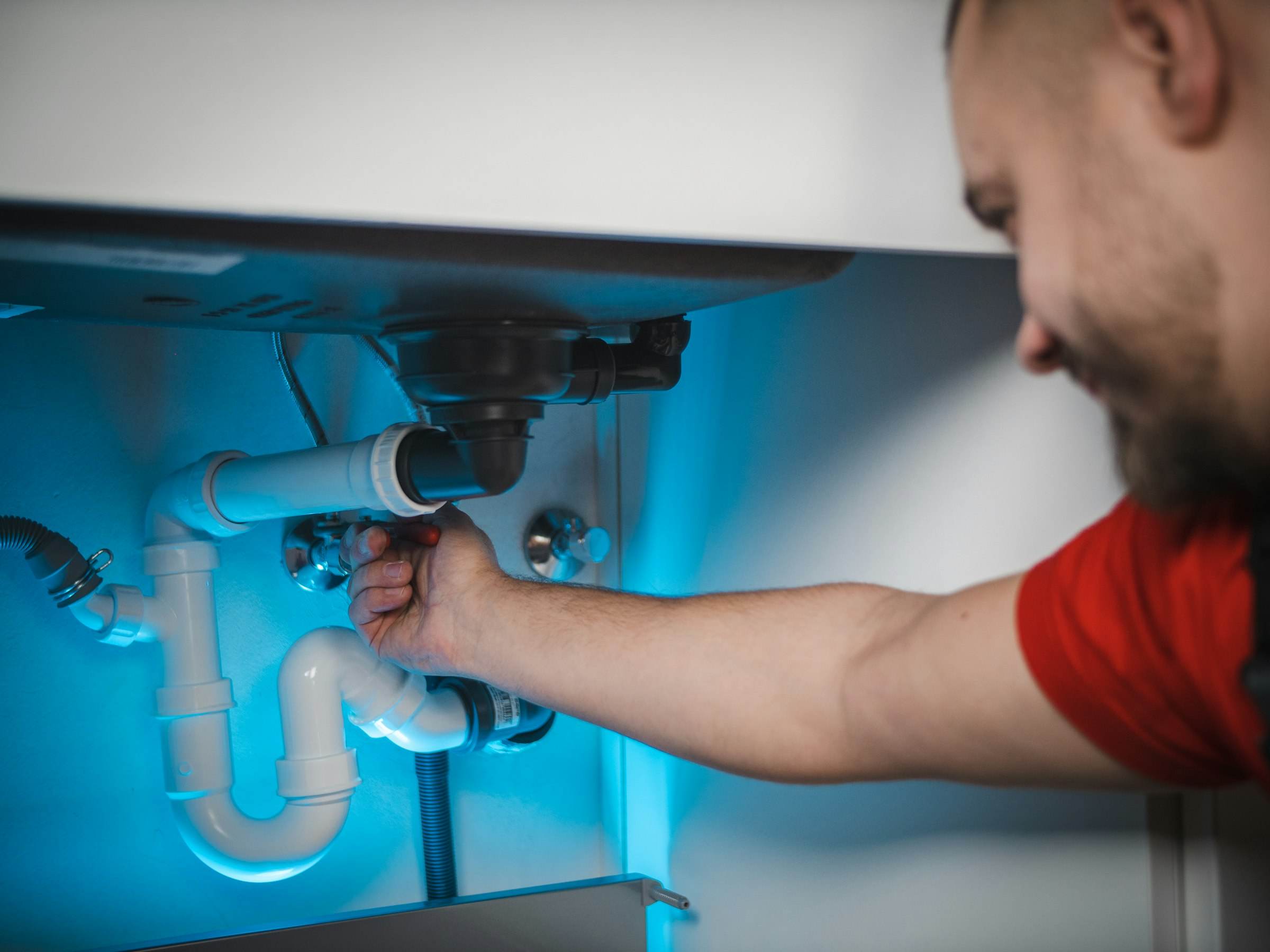 A plumber reaching under a sink to fix a drain trap