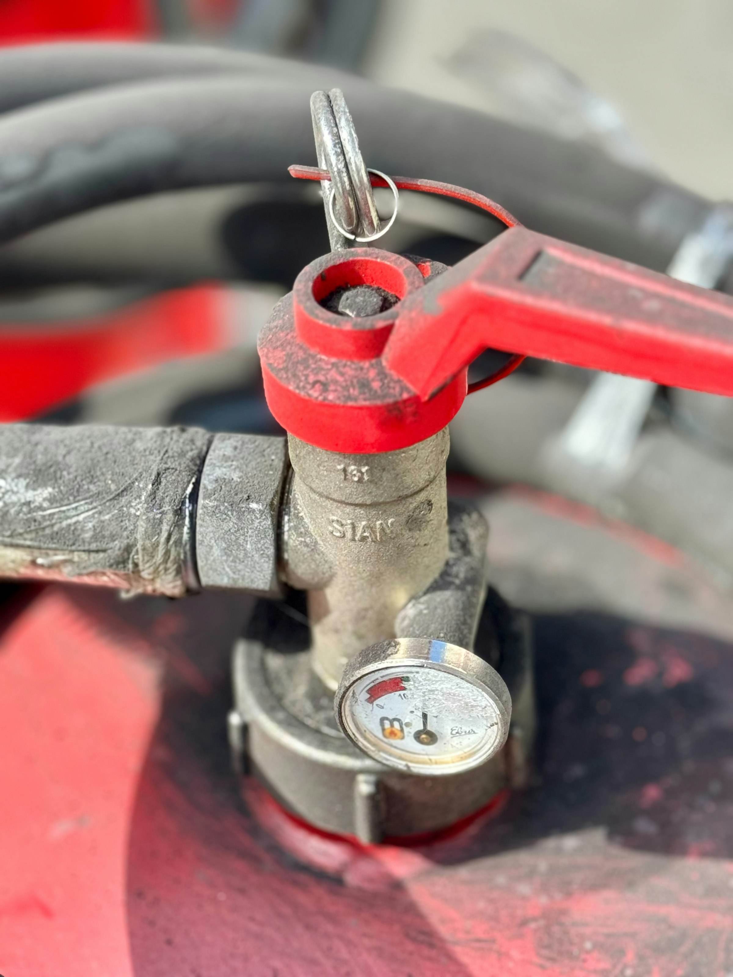 A red shut-off valve with a pressure gauge, close up